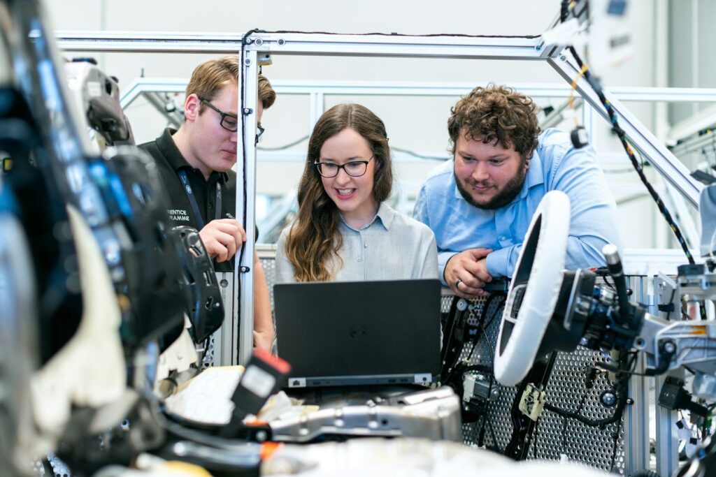 Trois ingénieurs regardant un ordinateur portable à côté d’équipements dans un atelier